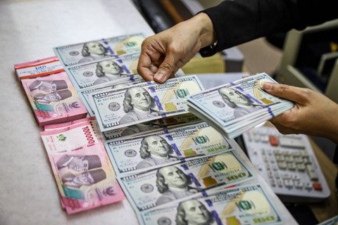 Seorang petugas menunjukan pecahan Dolar AS dan Rupiah di salah satu tempat penukaran mata uang asing di Kwitang, Jakarta, Senin (9/12/2024). Foto: kumparan